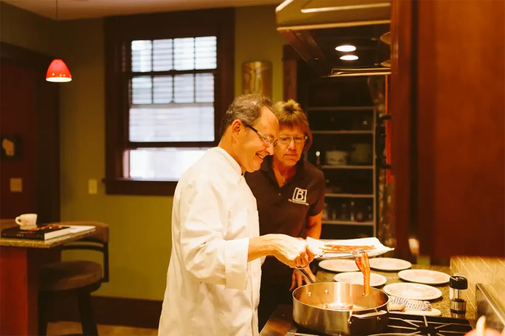 Innkeeper and chef cooking crispy bacon in a cozy kitchen, showcasing the personalized hospitality and home-cooked meals at The Buckingham Inn.